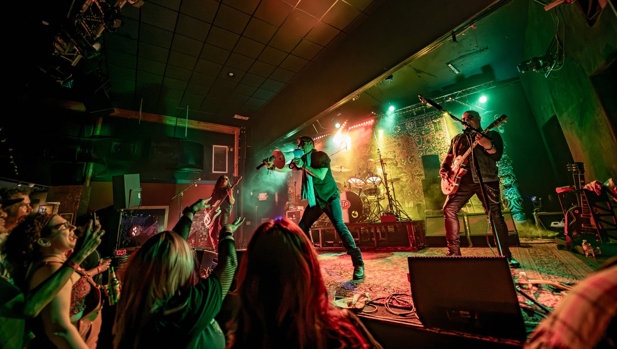 San & Tone Pilots performing live under green and gold stage lights, with the crowd in the foreground